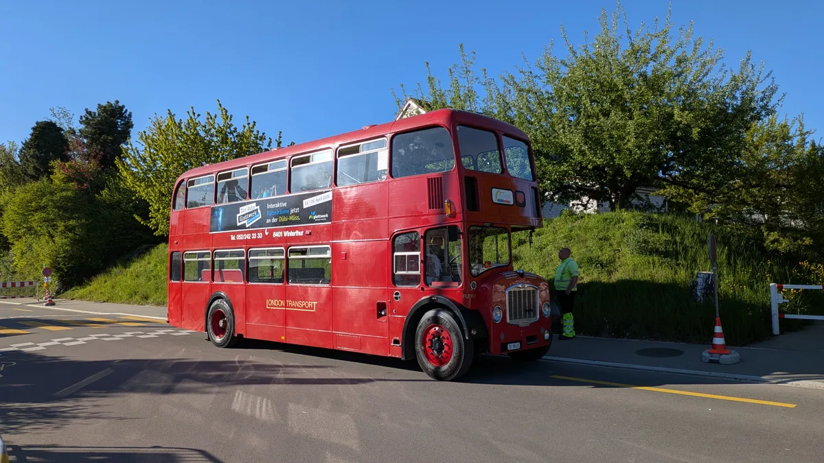 Ein roter Doppeldeckerbus hält an der Strasse.